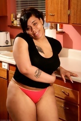 Big lady with tattoo on right chest poses naked in the kitchen