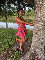 Bold babe in pink dress and white bikini poses solo by trees and lake
